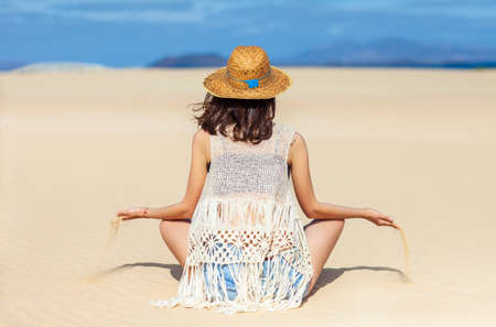 Back view of young hippie woman sitting in desert and holding sand let it running through fingers. Time running, lost conceptの写真素材