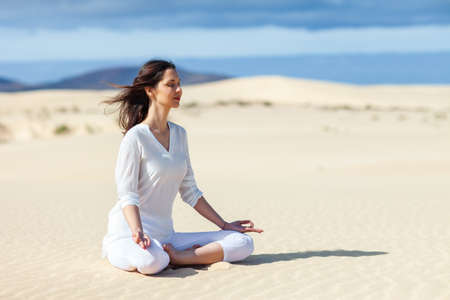 Young woman meditating in Lotus Pose in desert on Canary Islands, Spain. Padmasana. Relax conceptの写真素材
