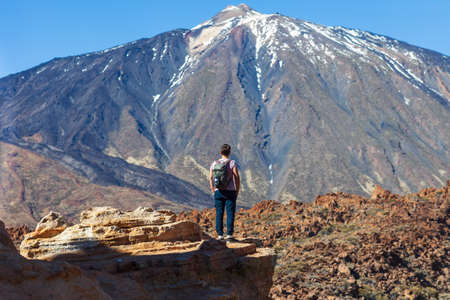 Back view of traveler man standing on the edge of rock looking to volcano El Teide in National park of Tenerife, Canary Islands, Spain. Travel the worldの写真素材
