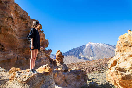 Young woman standing on the edge of rock looking to volcano El Teide in National park of Tenerife, Canary Islands, Spain. Travel destinationの写真素材