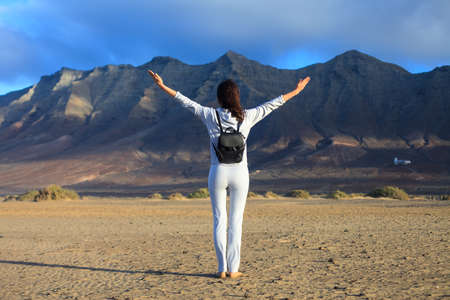 Freedom traveler woman with raised arms enjoying fantastic view of mountains range in Canary Islands, Spain. Travel destination. Success concept. Full length portraitの写真素材