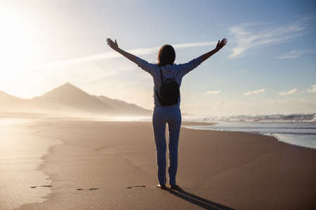 Back view of happy woman with hands up enjoy ocean beach, Canary Island, Spain. Summer vacation concept. Travel backgroundの写真素材