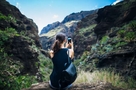 Young woman taking photo of mountains landscape using phone, Canary islands Spain. Travel conceptの写真素材