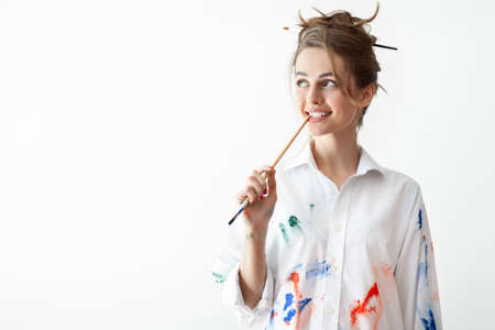 Beautiful young woman biting brush in thoughts with copy space. Doubt and wonder conceptの写真素材