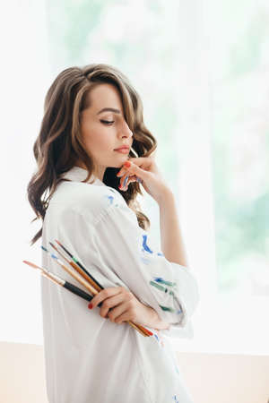 Beautiful thoughtful woman artist with brushes posing in her studio. Beauty conceptの写真素材