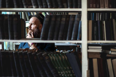Portrait of bearded thoughtful man strokes beard in bookstore backgroundの写真素材