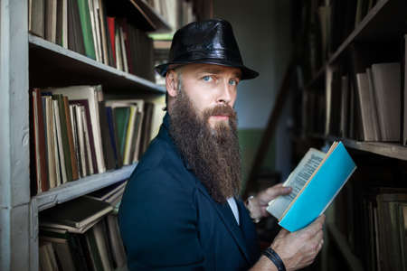 Stylish bearded man with book in library. education, university conceptの写真素材