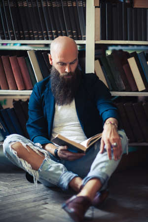 Handsome bearded man sitting on floor, reading book and relaxing in library or bookstoreの写真素材