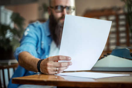 Bearded stylish writer reading his novel. Modern writer in glasses working on new book in libraryの写真素材