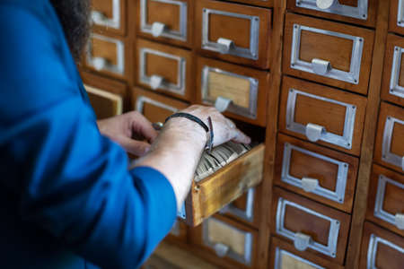 Man's hand searching for files into library or archive reference card catalog, close upの写真素材
