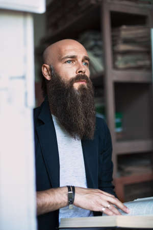 Portrait of bearded thoughtful man with book in libraryの写真素材
