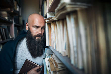 Dramatic portrait of tired bearded hipster man in stress in library. Depression conceptの写真素材