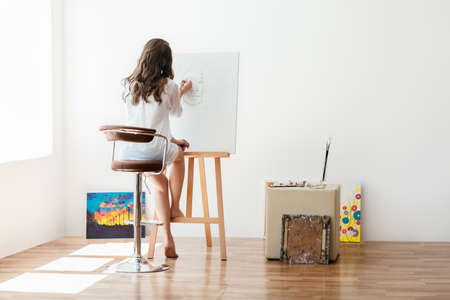 Rear view of young female artist painting on canvas in studioの写真素材
