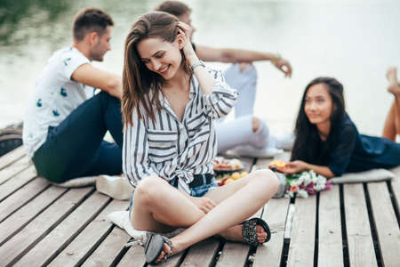 Young beautiful woman relaxing by river in company of friends. Vacation conceptの写真素材