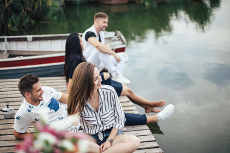 Group of happy young friends relaxing on river pier. Summer vacation conceptの写真素材