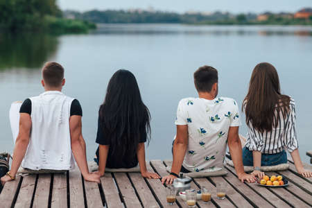 Back view of friends relaxing on river pier. Summer vacation conceptの写真素材