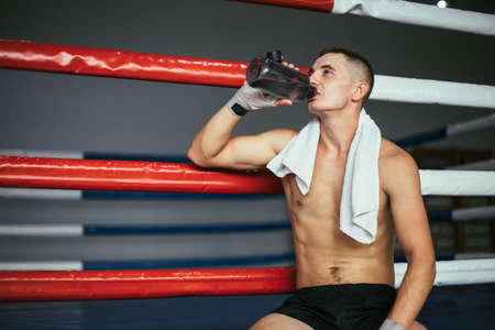 Male boxer drinking water after fight or workout exercising in boxing ringの写真素材