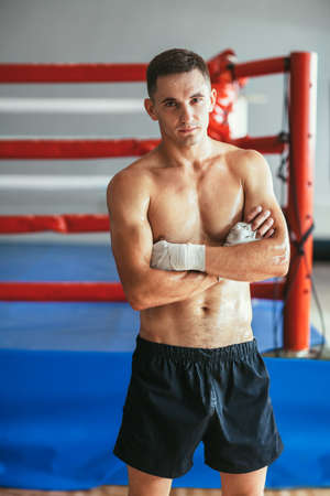 Portrait of muscular handsome boxer on ring background. Man with arms crossed and naked torso posing...
