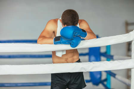 Tired boxer resting in boxing ring, head on gloves. Break in battleの写真素材