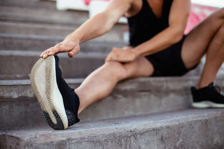 Young man stretching in stadium stairs before running, focus on shoesの写真素材