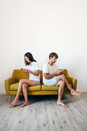 Young couple sitting on sofa back to back using mobile phones. Problem in relationship