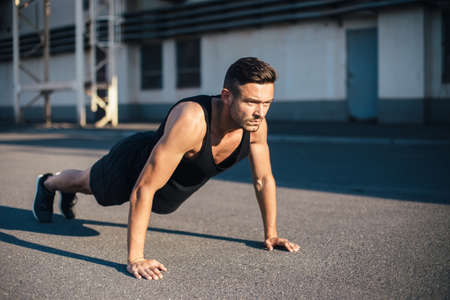Young serious man doing pushups outdoor on industrial background. concentrated sportsman doing...