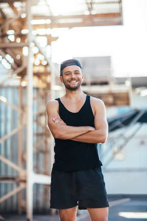 Happy smiling sportsman with crossed arms on industrial background. Success and healthy lifestyle conceptの写真素材