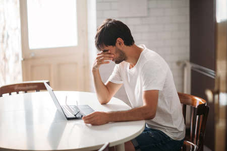 Young tired man in stress working on laptop at home