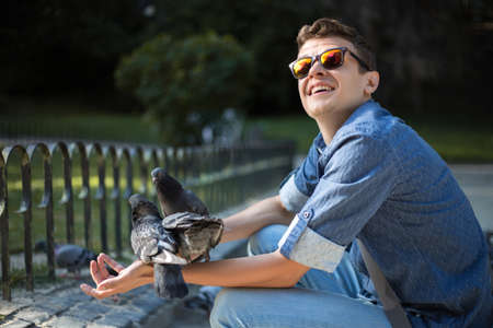 Happy man holding and feeding pigeons in the park outdoorの写真素材