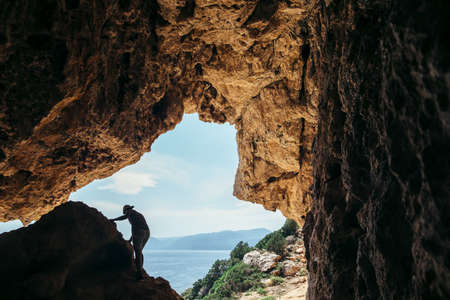 Male rock climber silhouette on a cliff in a cave against beautiful sea landscape