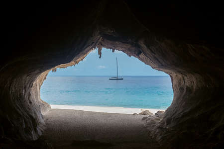 Exit from the cave overlooking beautiful sea and boat at Cala Luna beach, Sardinia island, Italy