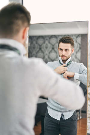 Handsome young man adjusting a tie in front of the mirror. Shopping, fashion, style and people...
