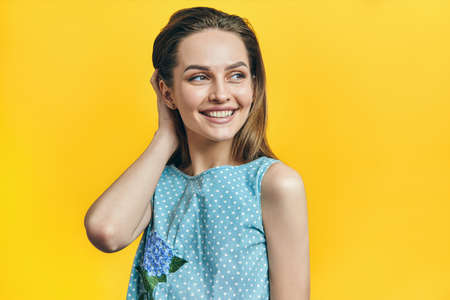 Portrait of beautiful sexy woman touching her hair and smiling, on yellow backgroundの写真素材