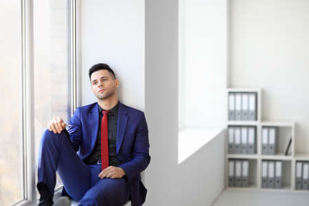 Tired businessman sitting on window sill at office