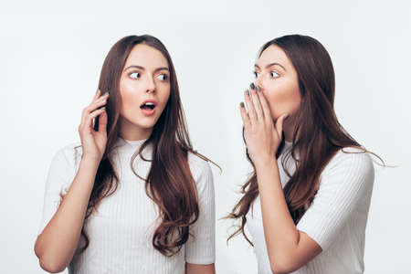 Two sisters twins gossiping isolated on white background. Share secret concept