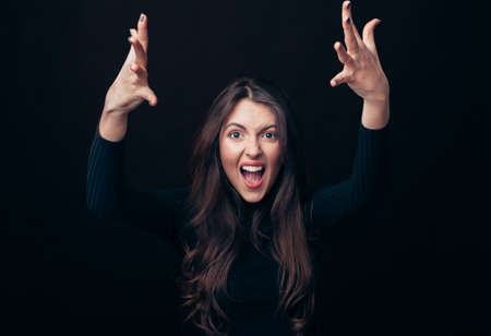 Screaming emotional angry woman with arms up isolated on black background. Negative emotions, hate, rage or stress conceptの写真素材