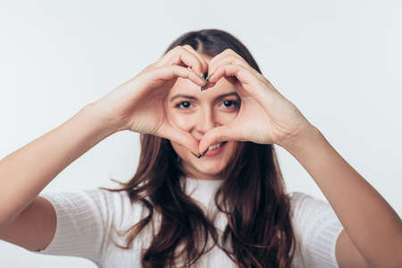 Beautiful happy woman making heart shaped symbols with her hands over white background. Love and...