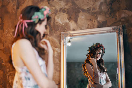 Beautiful young woman looking at her reflection in the mirror.  Girl dressing concept             の写真素材