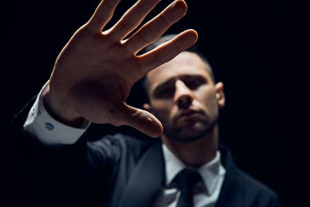 Handsome man in suit showing stop sign isolated on dark backgroundの写真素材