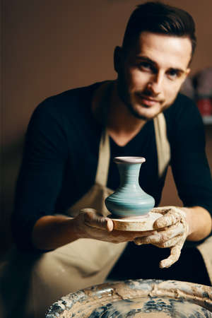 Smiling handsome man showing handmade ceramic pot at pottery workshop. Art conceptの写真素材
