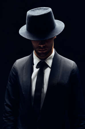Handsome confident man in black suit and hat on dark background. Man beauty conceptの写真素材