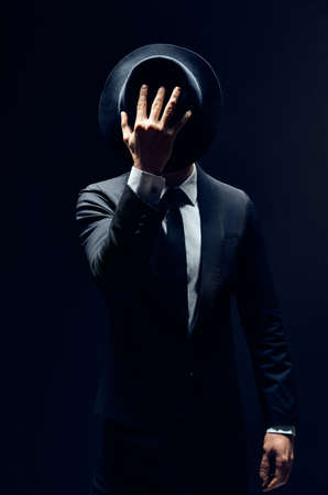 Man in suit hiding face behind his hat isolated on dark background. secret and incognito conceptの写真素材