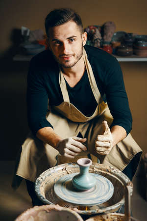 Smiling handsome man showing handmade ceramic pot at pottery workshop. Art conceptの写真素材