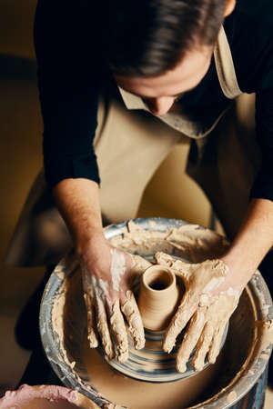 Man potter working on potters wheel making ceramic pot from clay in pottery workshop. art concept