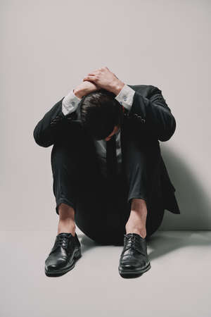 Depressed business man sitting on floor head in hands on white background. problems and  dramatic conceptの写真素材