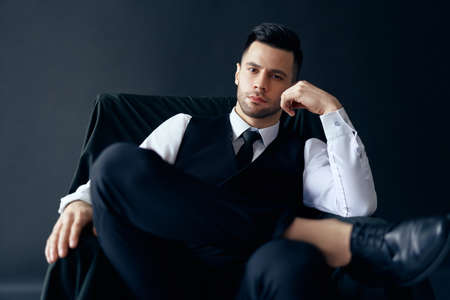 Confident thoughtful man in elegant suit posing sitting in chairの写真素材