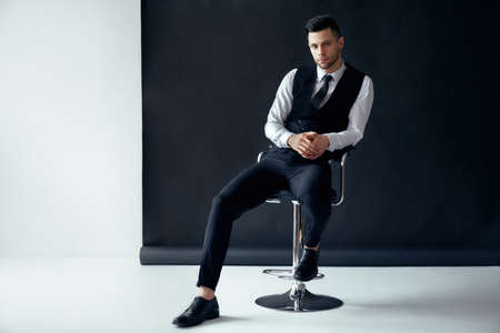 Elegant confident man posing and sitting on chair on black and white backgroundの写真素材