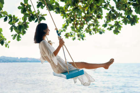 Carefree happy woman on swing on beautiful paradises beach. Relax and freedom conceptの写真素材
