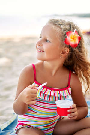 Cute blonde little girl eating ice cream on sandy beachの写真素材