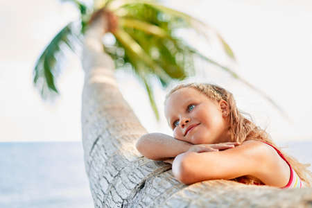 Happy dreaming beautiful child relax on tropical beach with palm treeの写真素材